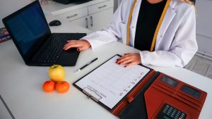Dietitian working on meal plan with laptop, fruits, and calendar for health consultation.